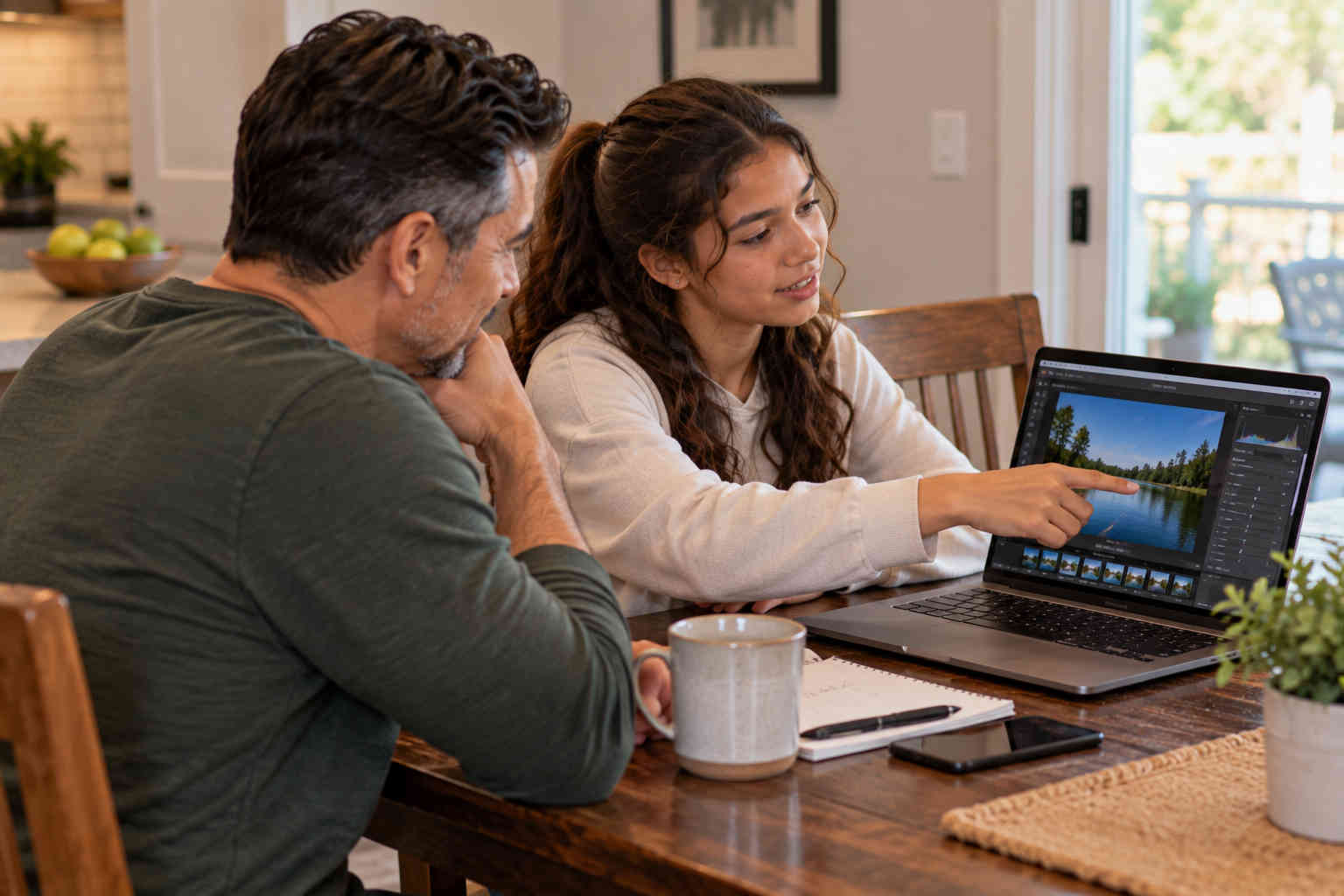 Daughter teaching her father how to edit a photograph on a laptop while both look at the screen
